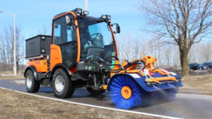 Holder C70 compact tractor with broom and sprayers clearing a park trail
